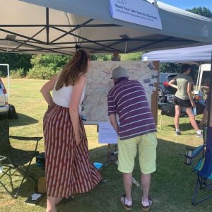 A man and a woman look at a big map on an easel, under a gazebo on a sunny day